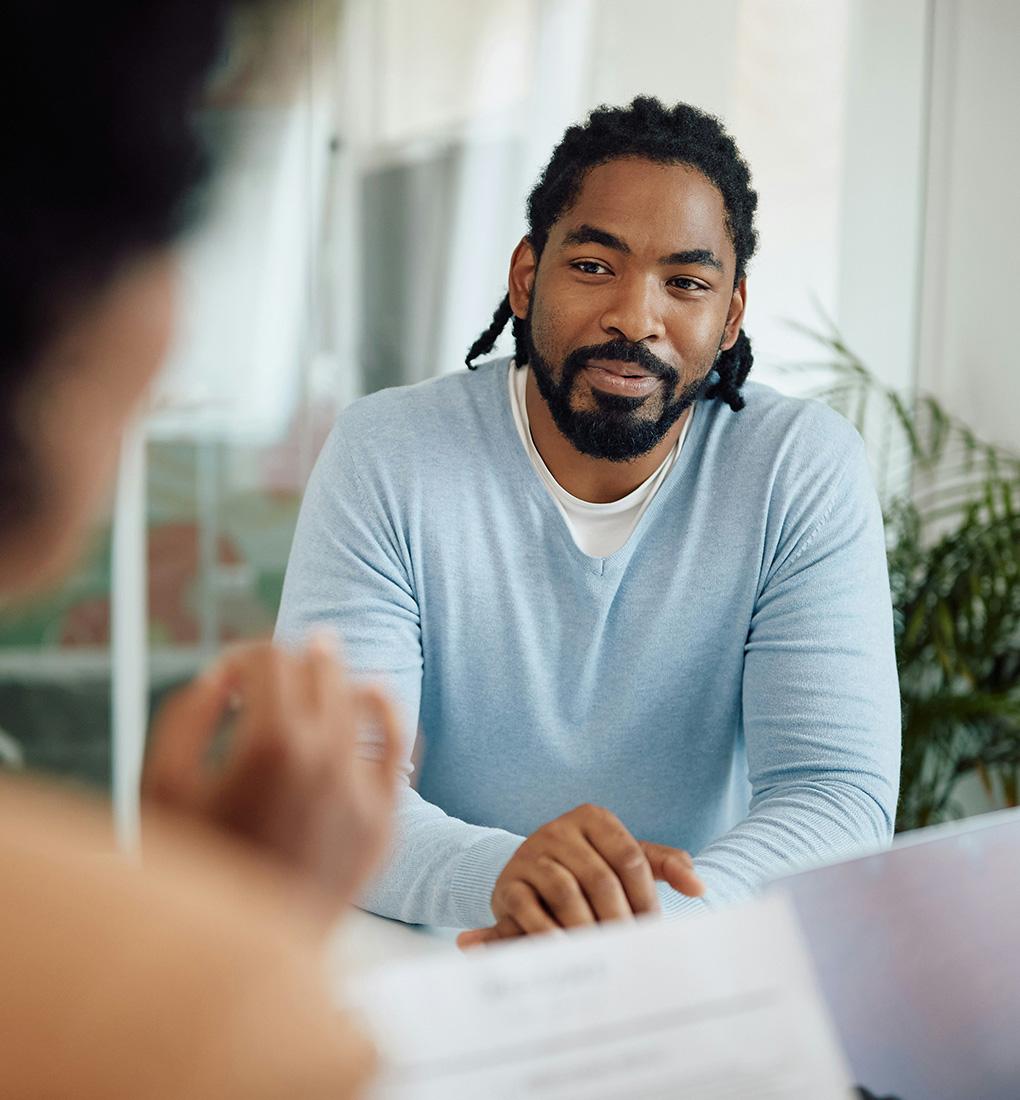 Man wearing a blue jumper in an office board room interviewing for a job.